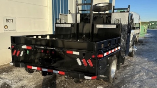the black deck of a white truck from behind, with custom toolboxes on either side behind the cab.